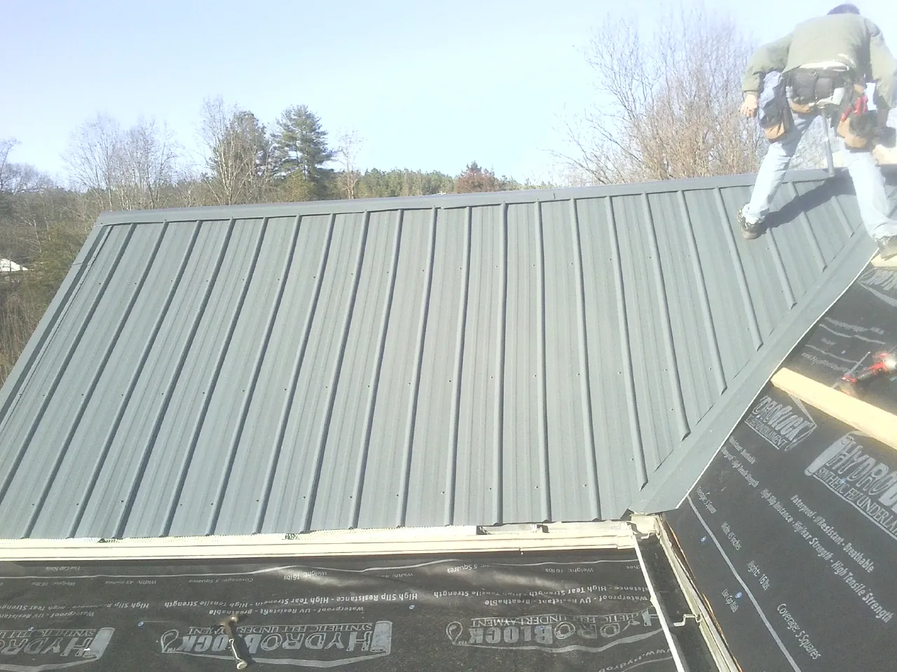 Crew installing dark green standing seam panels over synthetic underlayment in Fayetteville