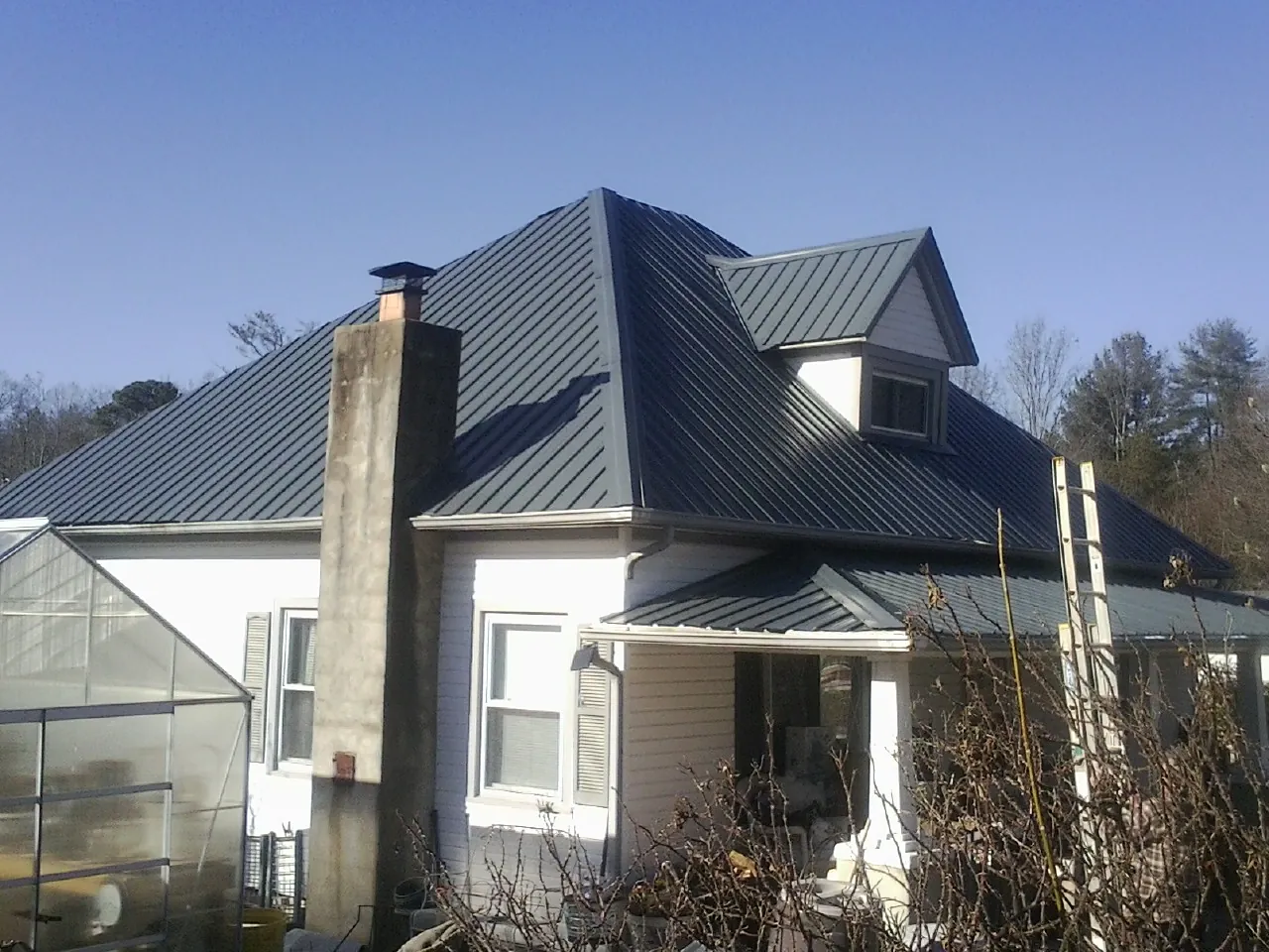 Dark blue standing seam metal roof on a white farmhouse with dormer — Slate & Tile Roof Repair by Roofing Brothers in Fayetteville
