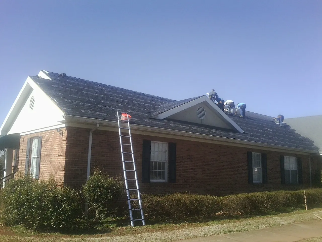 Crew tearing shingles off a brick ranch roof with a ladder set — Metal Roof Repair work by our crew in Fayetteville