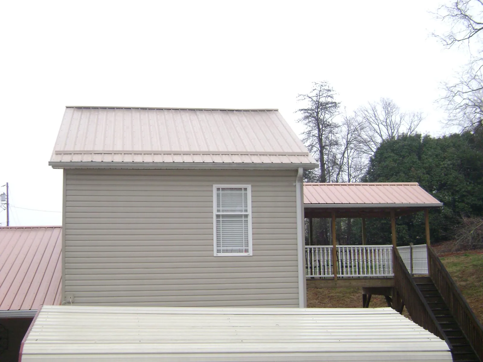 Tan metal roofs on a two story addition and attached porch, from a Roof Replacement job in Fayetteville